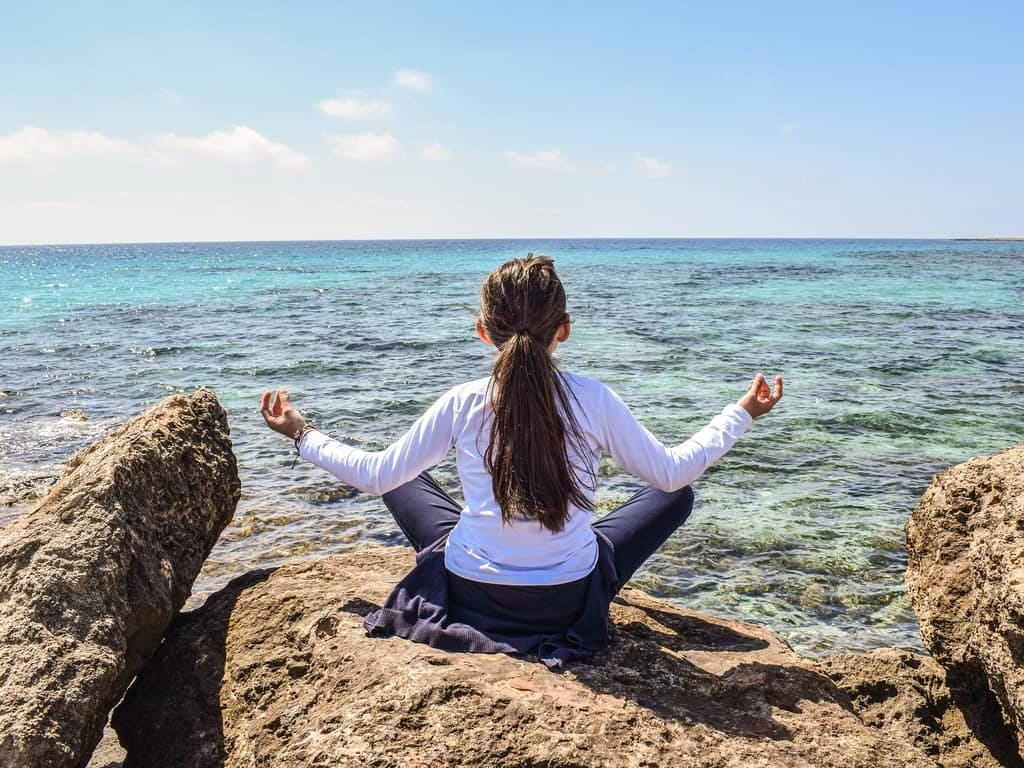 Woman meditating on rocks by the sea