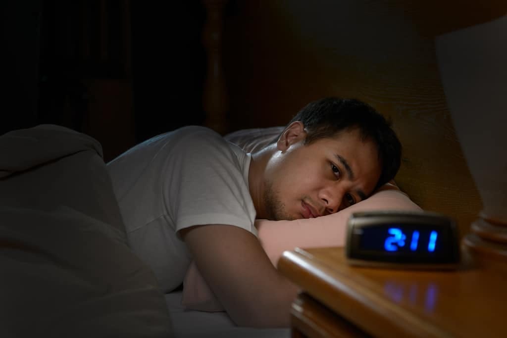 Man lying awake at night next to his alarm clock