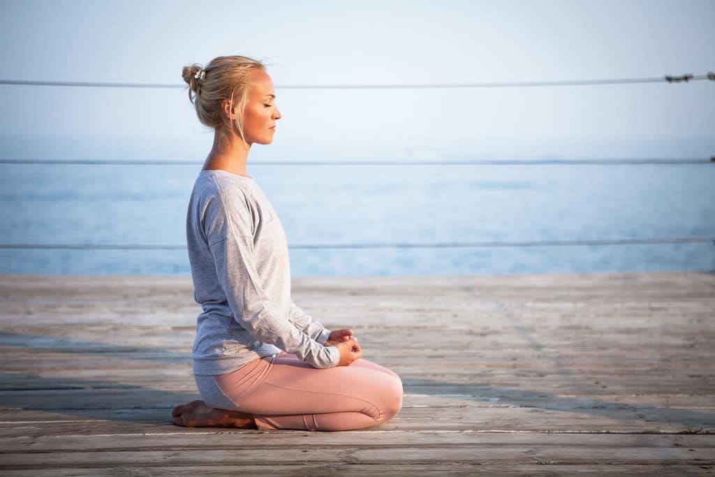 Woman meditating on a pier by the sea